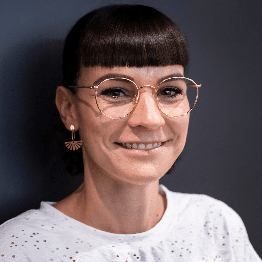 Frau mit Brille und Pagenschnitt lächelt.